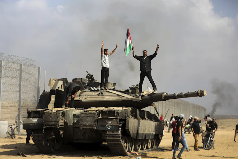 Dois homens, um empunhando a bandeira palestina, estão de pé sobre um tanque de guerra israelense