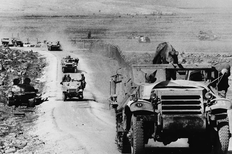 An armored vehicile drives down a dustry track with other behind it.