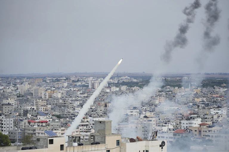 A rocket with a trail of smoke soars over buildings