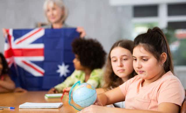 A child is looking at a globe with a teacher in the background holding an Australian flag.