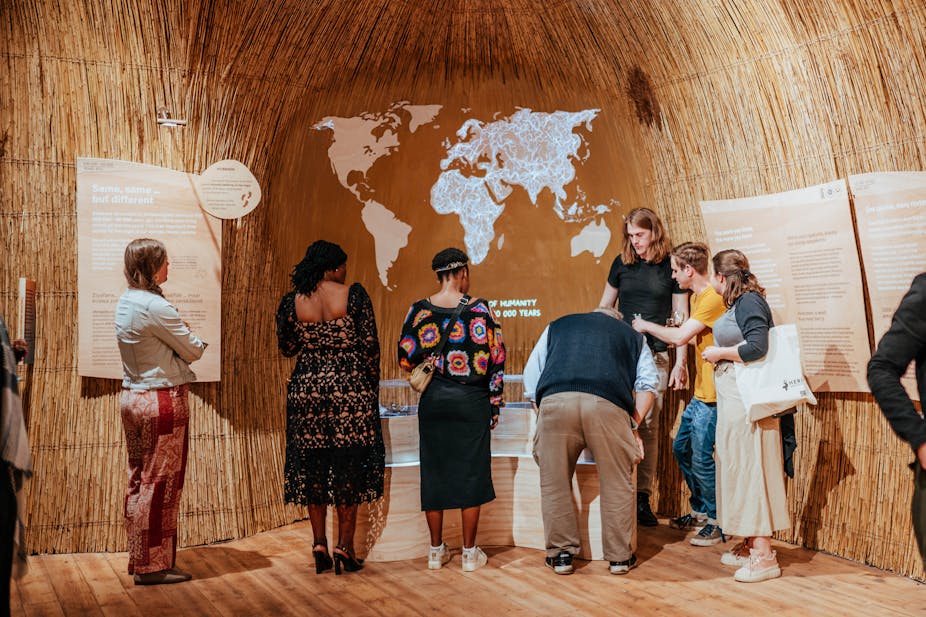 Seven people are pictured in a loose semi-circle, all reading or pointing at different elements of a display centered on a map of the globe