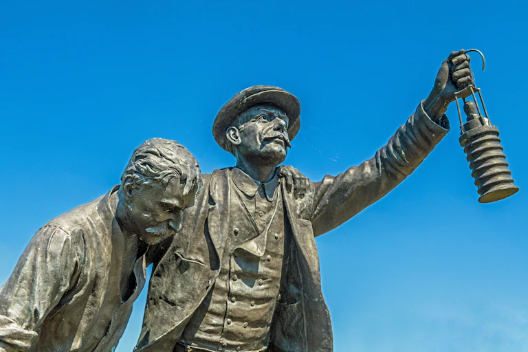 A statue of a man in a hat holding up a lamp.