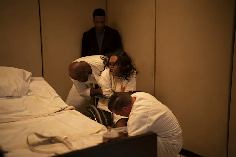 young girl struggles in hospital chair and is restrained by doctors