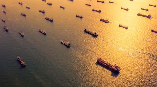 Sun shines on sea with many floating oil tankers.