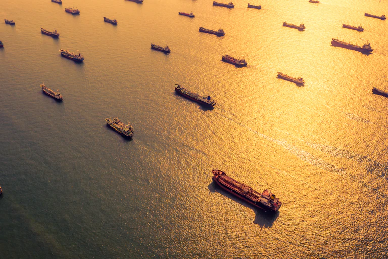 Sun shines on sea with many floating oil tankers.