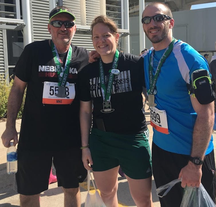 Man in his 60s, a middle-aged woman and a middle-aged man, all wearing race medals and running gear.