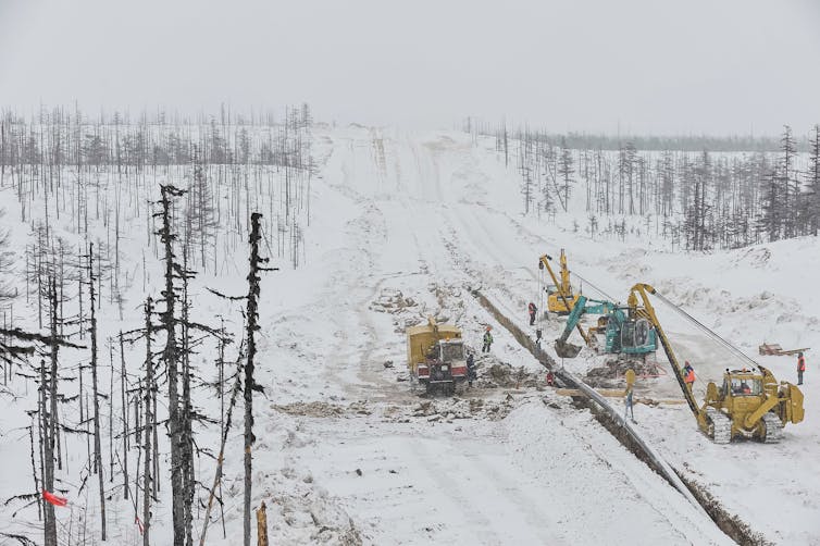 Snow, bare trees, machinery, pipeline, workers.
