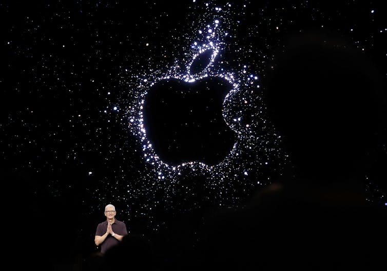 Apple CEO Tim Cook stands under a giant glittery Apple logo on a black background.