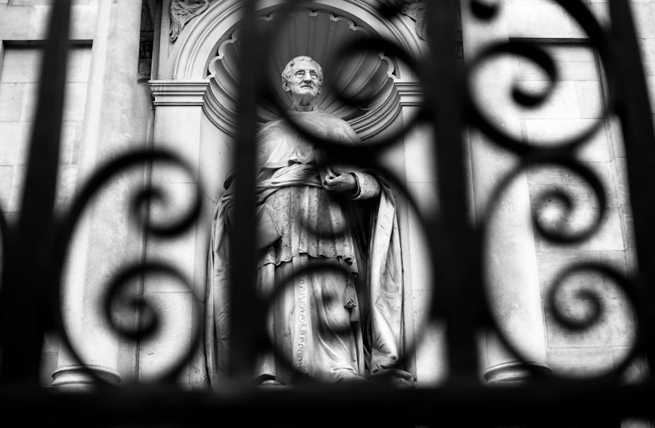 A black and white photo of a statue shot from behind an elaborate iron gate.