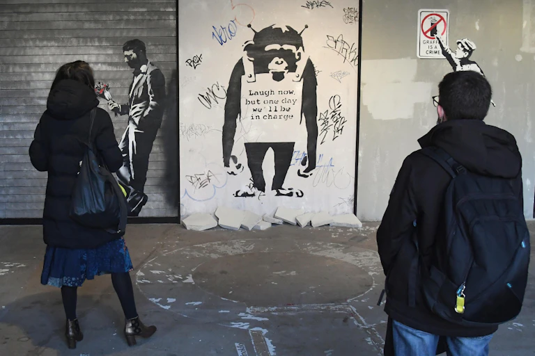 Two people look at Banksy's artwork of a monkey.