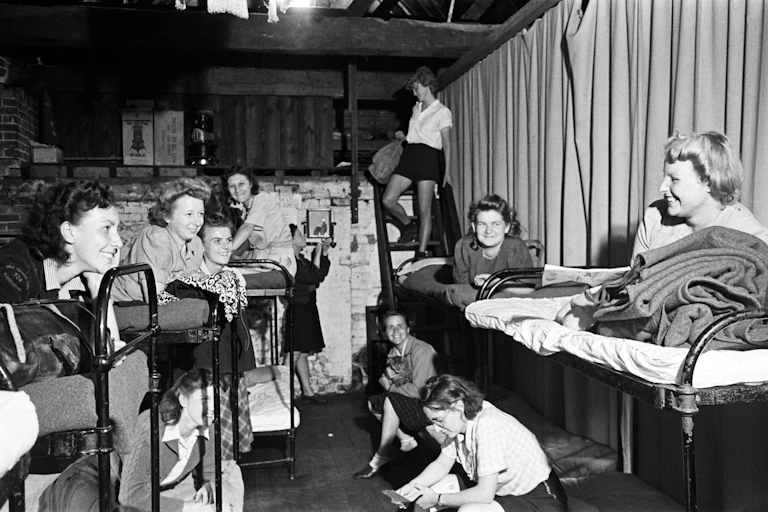 A historic photograph in black and white depicting young women gathered in a dormitory.