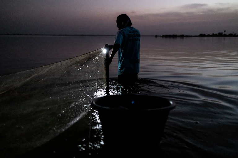 Un homme avec une torche allumée et une bassine jette son regard sur l'eau