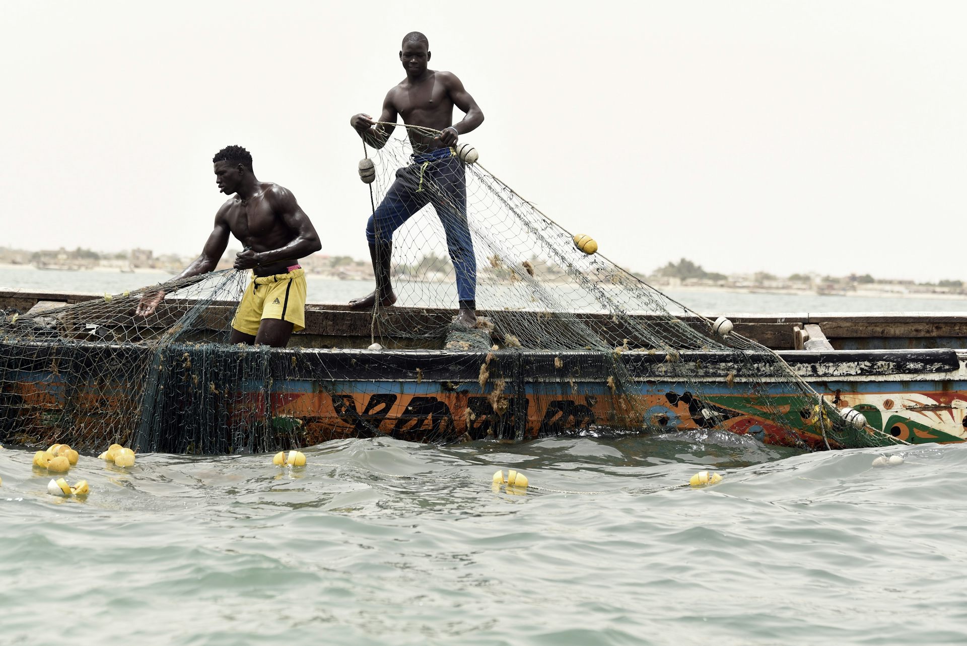 Deux hommes, le torse nu, tirent leurs filets de pêche