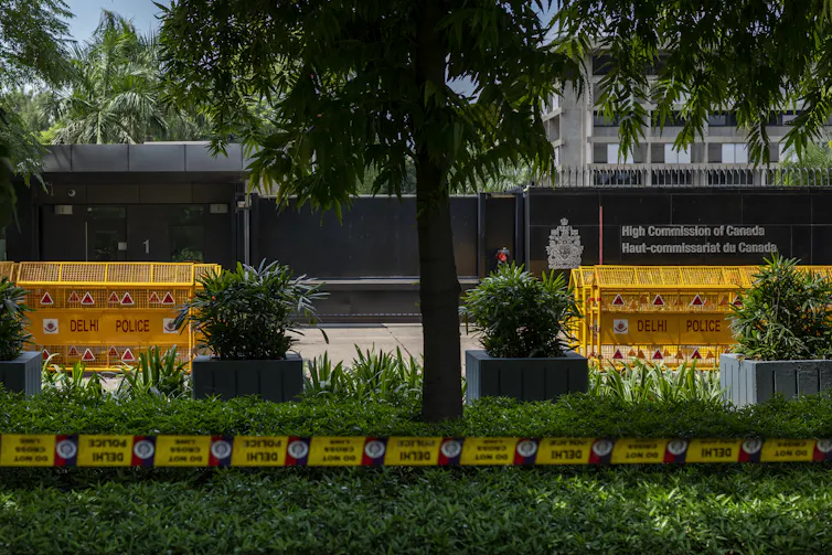 Yellow police tape and barricades in front of a government building with palm trees in front of it.