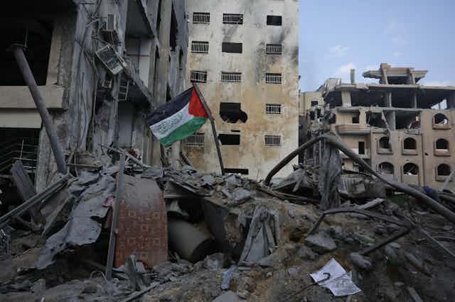 A green, red, black and white Palestinian flag stands out of rubble next to destroyed buildings.