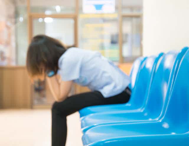 Out-of-focus photo of a woman with her head in her hands in a waiting room with blue chairs