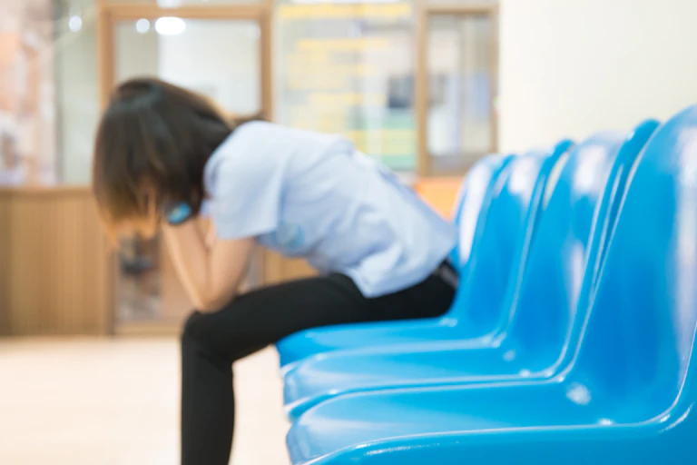 Out-of-focus photo of a woman with her head in her hands in a waiting room with blue chairs