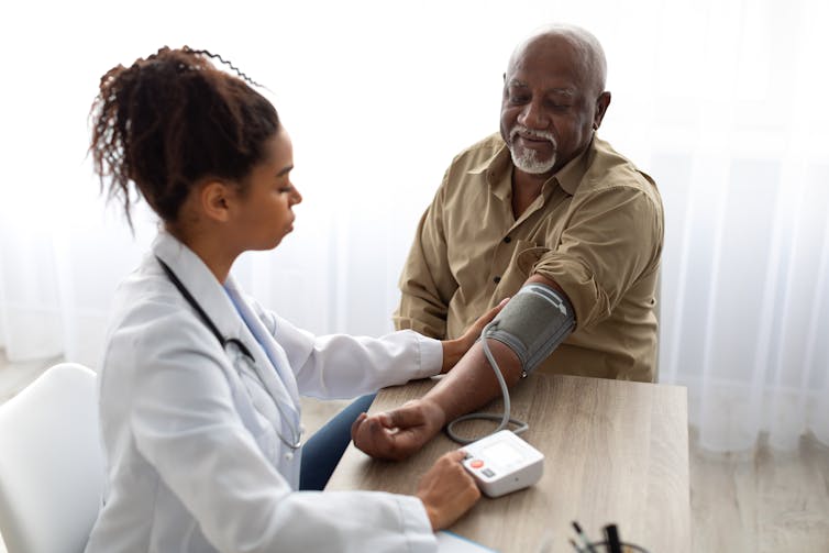 A woman in a white coat taking an older man's blood pressure