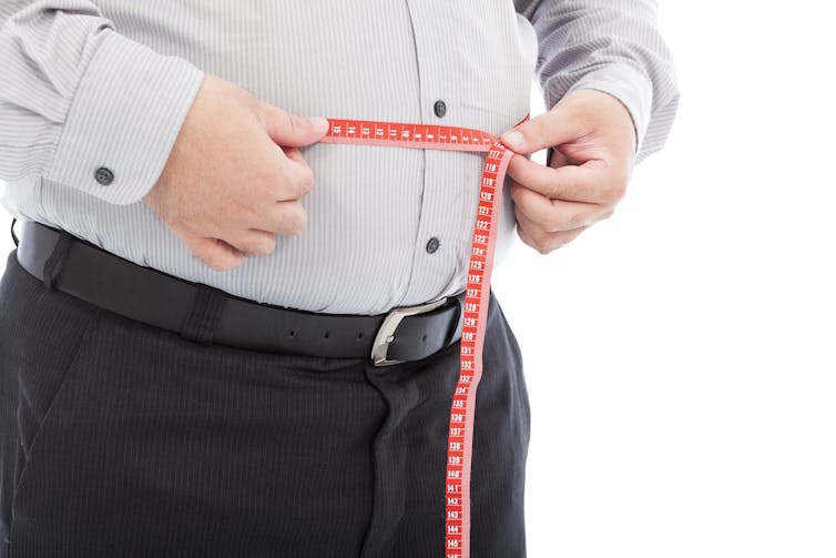 Un homme mesure son tour de taille avec un mètre de couture.