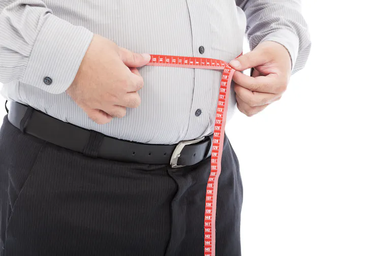 Un homme mesure son tour de taille avec un mètre de couture.