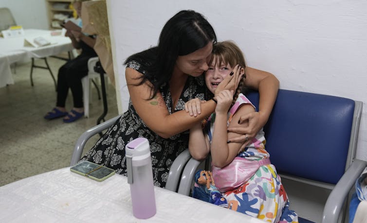 A child cries in fear as a woman embraces her.