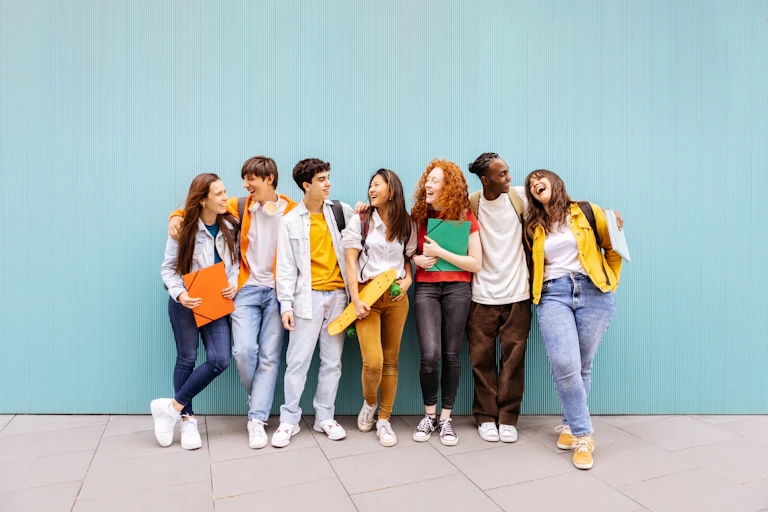 Un grupo de jóvenes se abrazan y ríen apoyados en una pared azul.