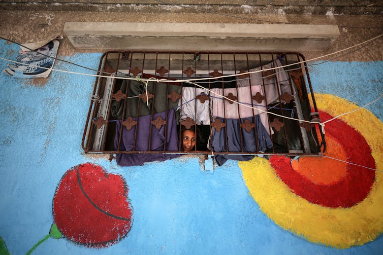 A blue, red and yellow mural on a wall in which there is a window through which a young boys looks.