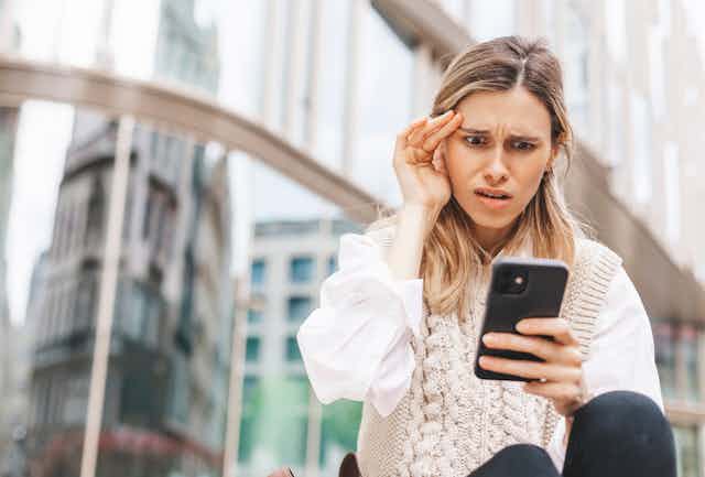 A young woman looks in shock at her mobile phone