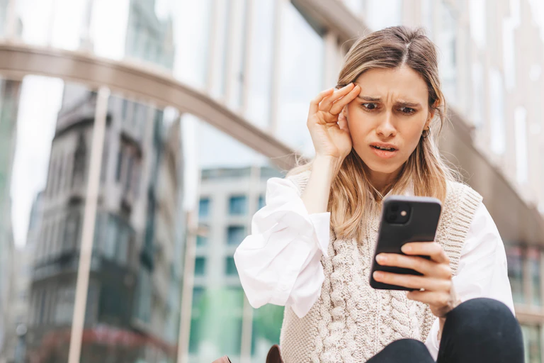 A young woman looks in shock at her mobile phone