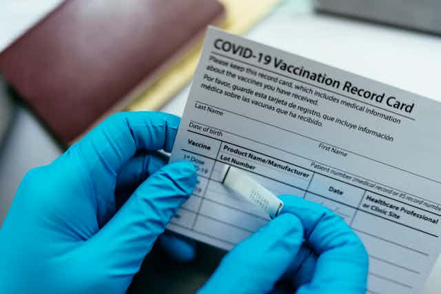 Gloved hands putting sticker on COVID-19 vaccination record card