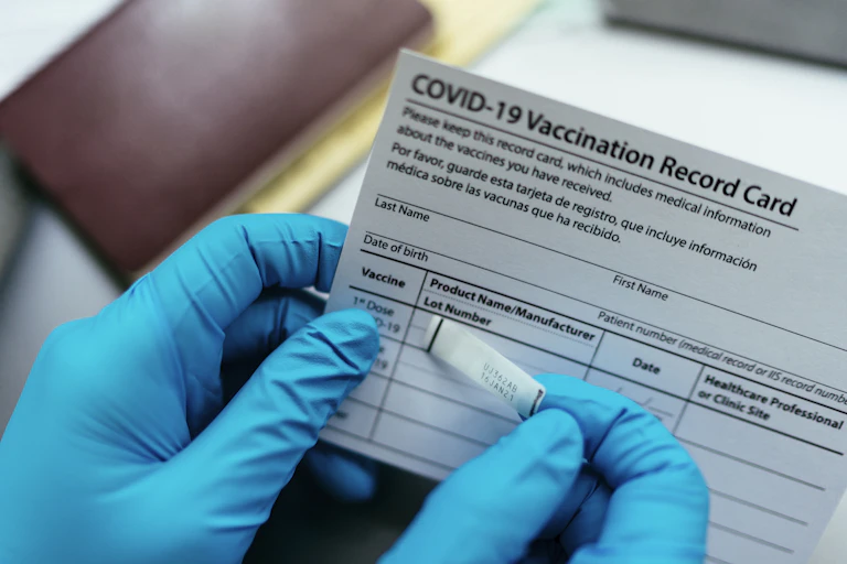 Gloved hands putting sticker on COVID-19 vaccination record card
