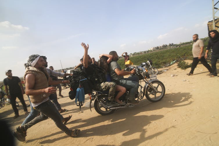 A motorcycle moves along, carrying two men with a young woman sandwiched between them.