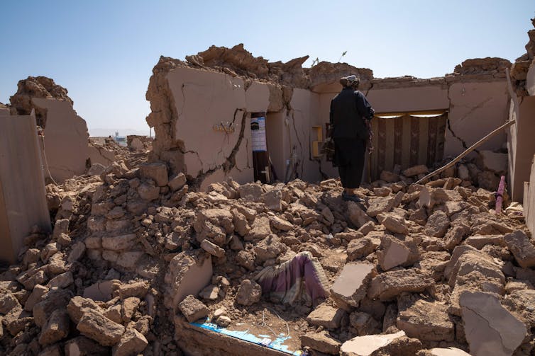 In a remote, rural setting, a man searches through the debris of what was once a home.