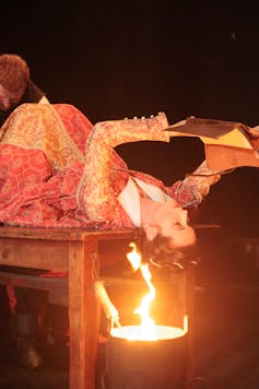 A woman reads over a fire.