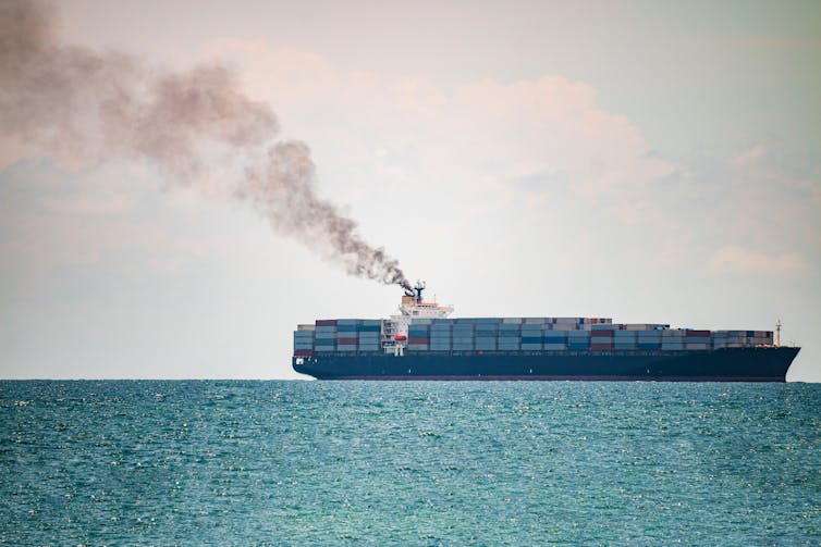 A container vessel spewing smoke on the horizon.
