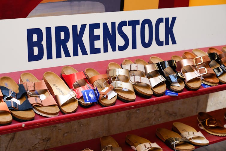 A shop shelf holding different Birkenstock styles and colours below a Birkenstock sign.