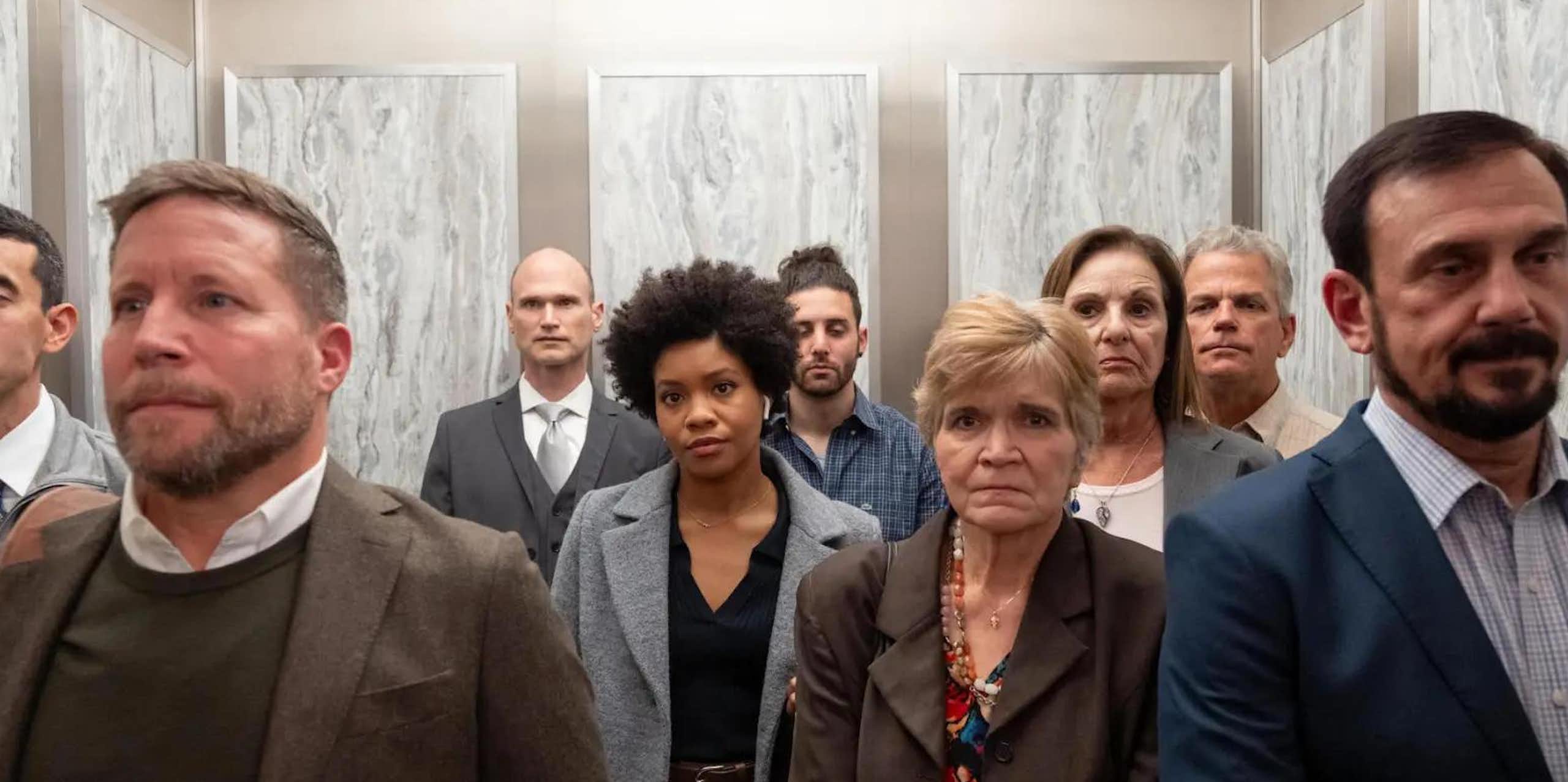 A Black woman stands in an elevator at work surrounded by white coworkers.