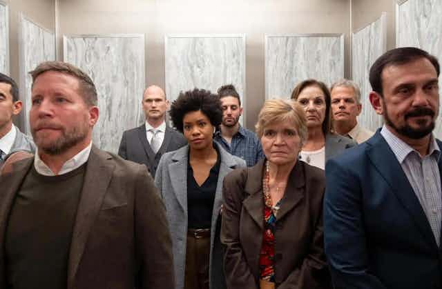 A Black woman stands in an elevator at work surrounded by white coworkers.