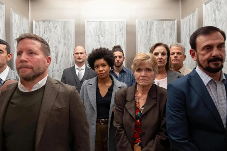 A Black woman stands in an elevator at work surrounded by white coworkers.