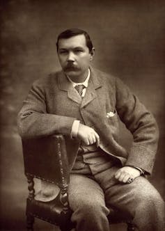 Arthur Conan Doyle in a suit sat on a chair.