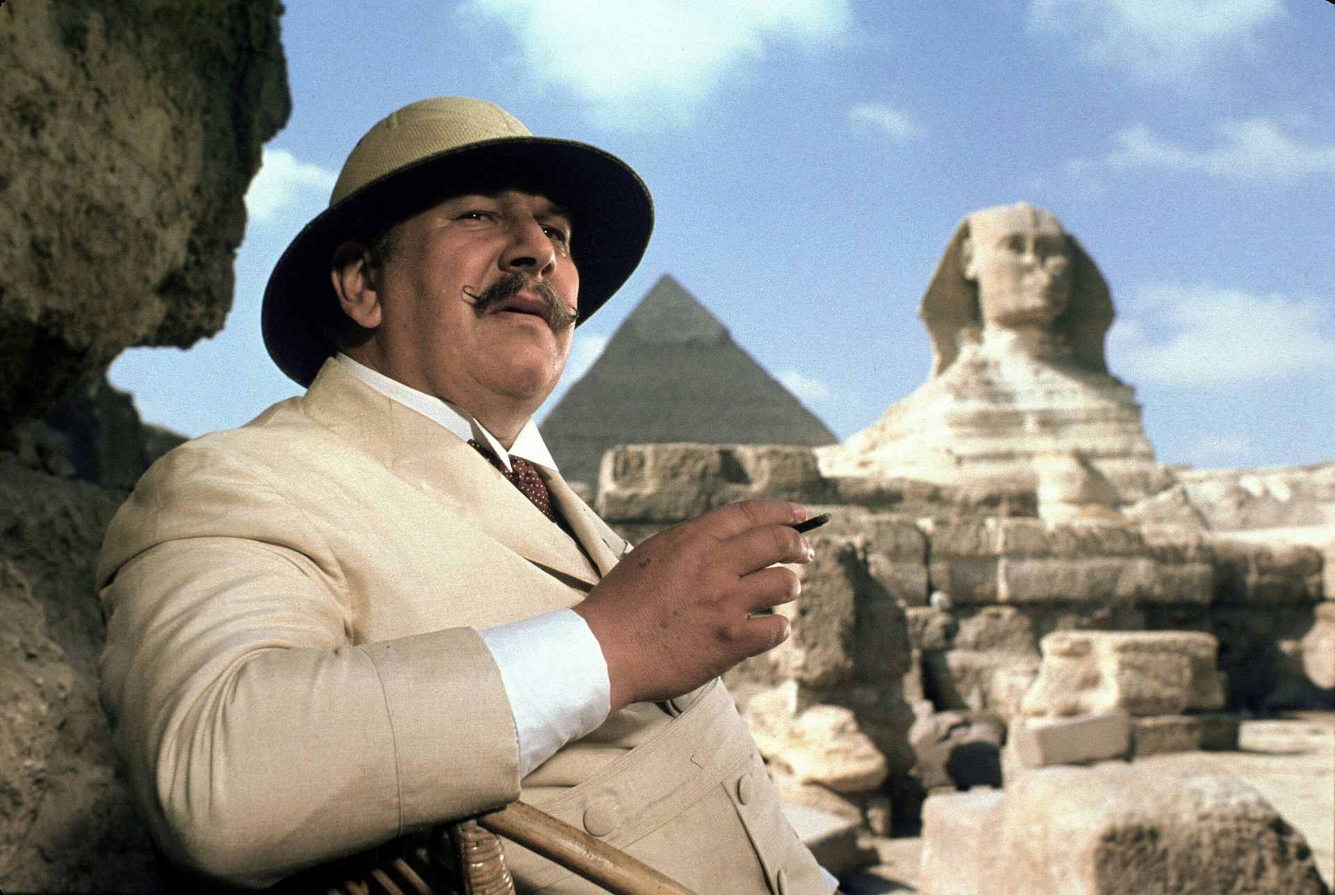 Peter Ustinov in pith helmet and cream suit, in front of Great Pyramid and Sphinx.