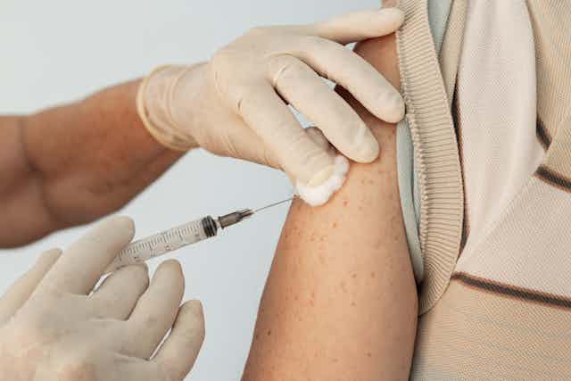 Closeup of nurse injecting a vaccine into the arm of an adult patient.