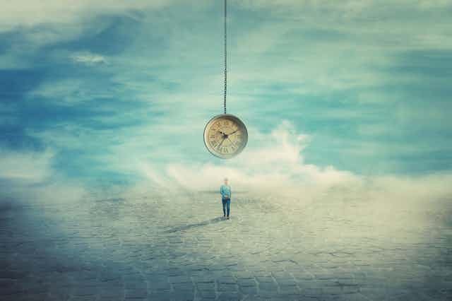 a man walks through a barren landscape, an analogue clock is suspended over him