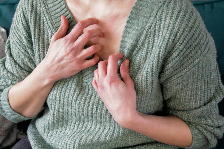Person lowering the collar of their sweater to scratch at their chest