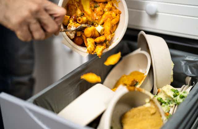Closeup photo of a person scraping leftover food into the rubbish bin, which will be sent to landfill