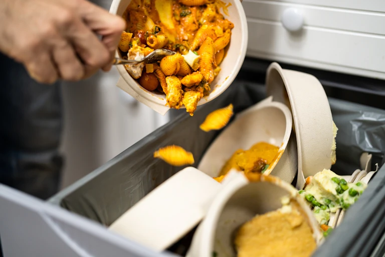 Closeup photo of a person scraping leftover food into the rubbish bin, which will be sent to landfill