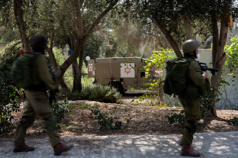 Deux soldats en vert tiennent des fusils et passent devant un véhicule médical portant une étoile juive.
