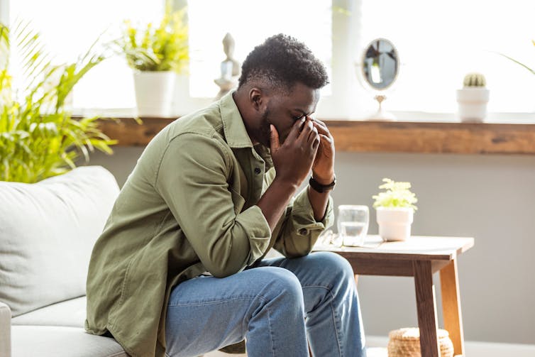 A man sitting on a couch appears stressed.