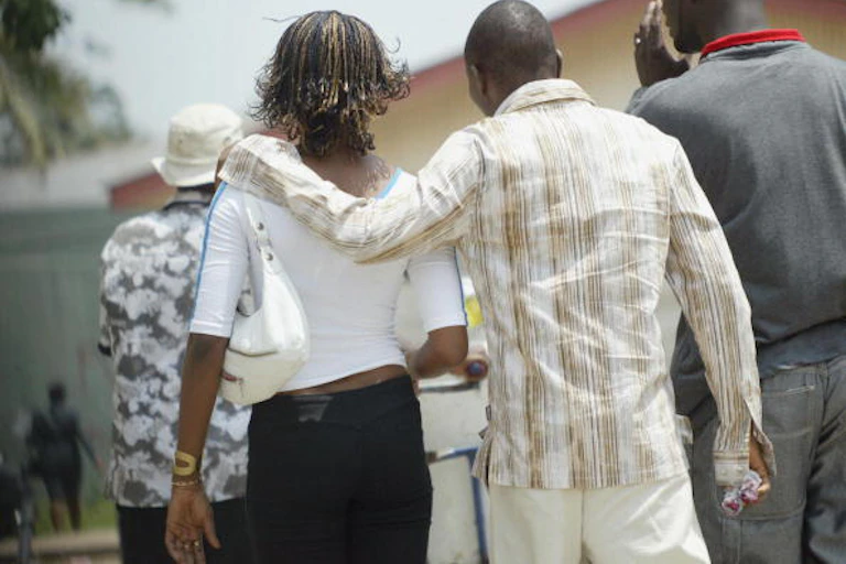 Seen from behind, a man has his hand on a woman's shoulder as they walk side by side.