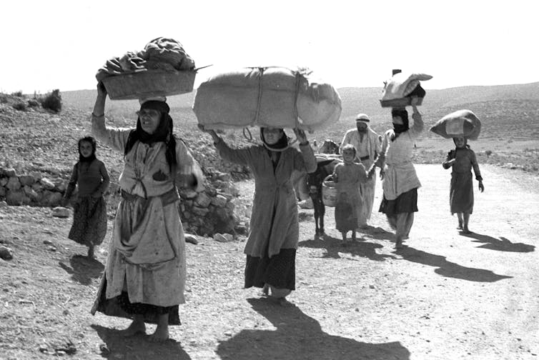 Hombres y mujeres árabes huyendo por una carretera con sus cosas sobre la cabeza.